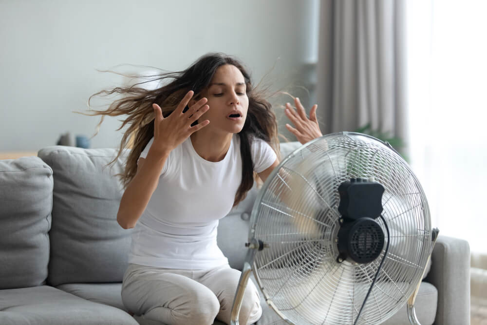 Tired woman in overheated room during UK heatwave highlighting need for portable air conditioning over basic fans Tired woman in overheated room during UK heatwave highlighting need for portable air conditioning over basic fans